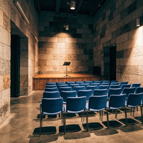Auditorium aux murs de pierre avec rangées de chaises bleues et pupitre