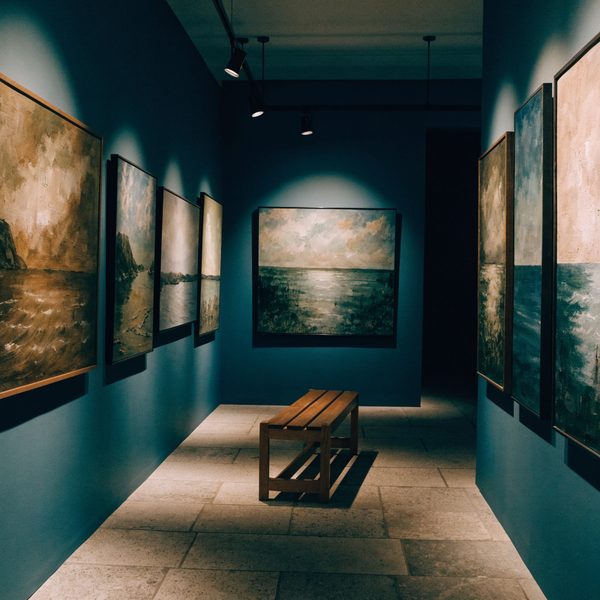 Salle d'exposition aux murs bleus, tableaux de marines éclairés, banc au centre